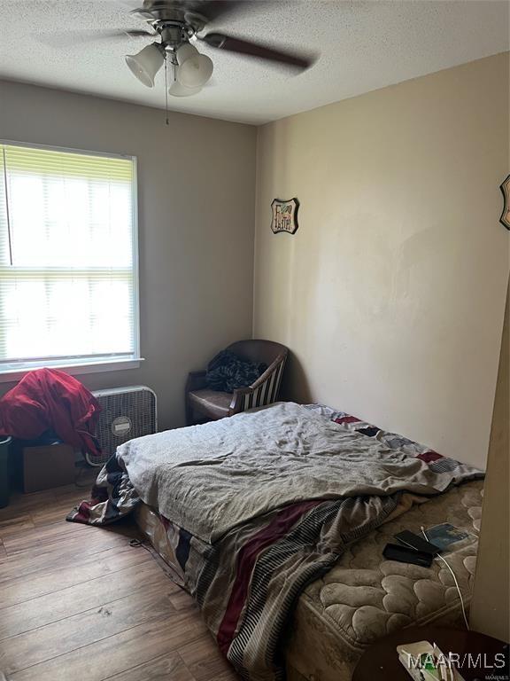 bedroom with ceiling fan, wood-type flooring, and a textured ceiling