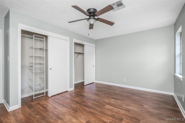 unfurnished bedroom with multiple closets, ceiling fan, and dark hardwood / wood-style flooring