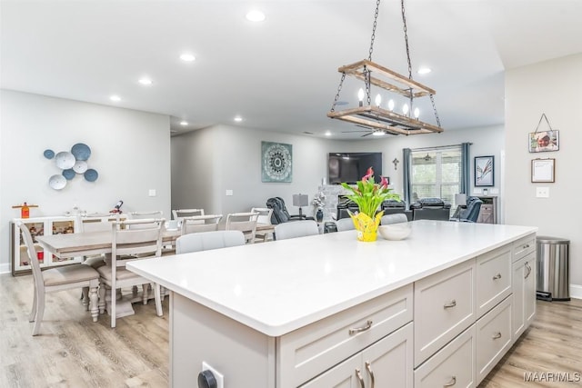 kitchen featuring hanging light fixtures, white cabinetry, a center island, and light hardwood / wood-style flooring