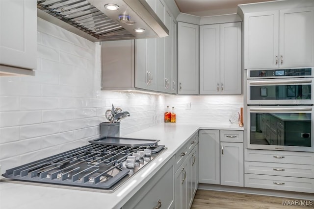 kitchen featuring appliances with stainless steel finishes, light hardwood / wood-style flooring, backsplash, and wall chimney exhaust hood