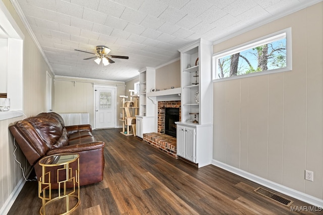 living room featuring built in features, ornamental molding, ceiling fan, a brick fireplace, and dark wood-type flooring