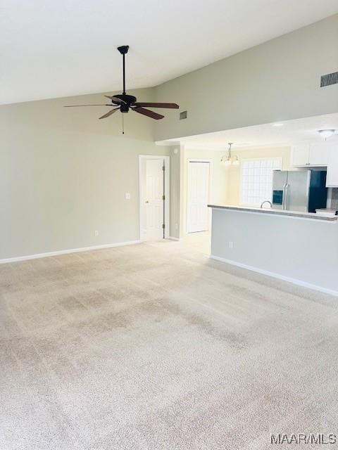 unfurnished living room with ceiling fan with notable chandelier, lofted ceiling, and light carpet