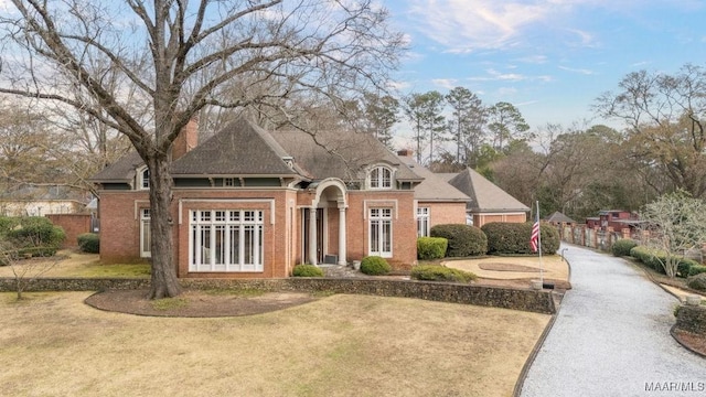 view of front of house featuring brick siding, a chimney, a front yard, and fence