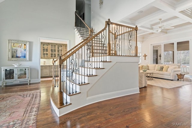 stairs with hardwood / wood-style floors, beamed ceiling, coffered ceiling, ceiling fan, and crown molding