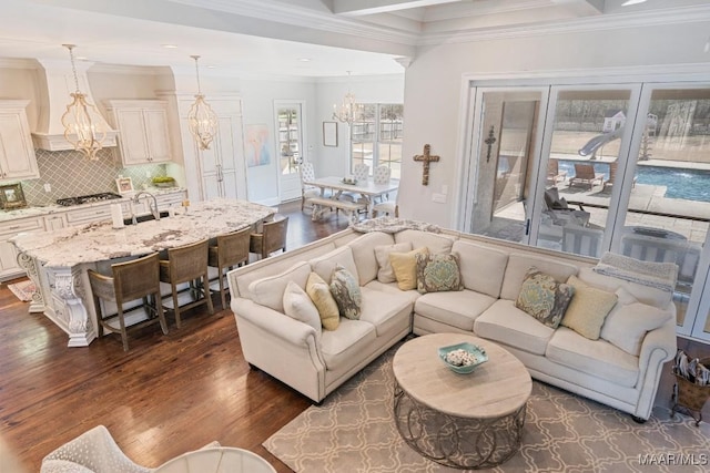 living room with dark hardwood / wood-style flooring, crown molding, sink, and an inviting chandelier