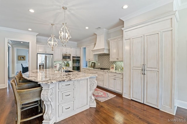 kitchen featuring premium range hood, sink, a center island with sink, appliances with stainless steel finishes, and pendant lighting