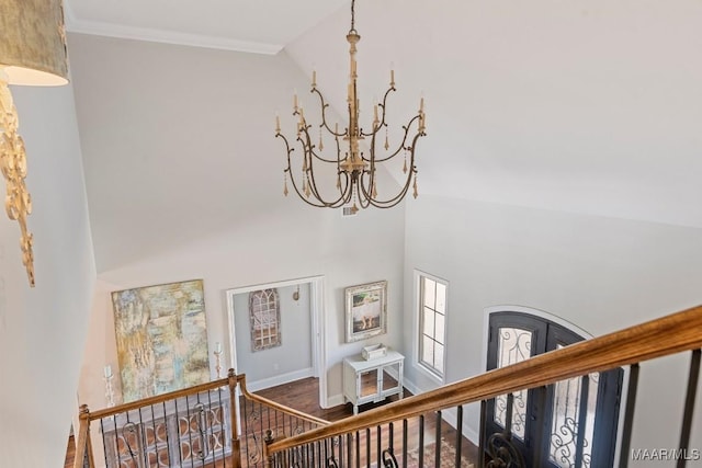 staircase with an inviting chandelier, wood-type flooring, ornamental molding, and a high ceiling