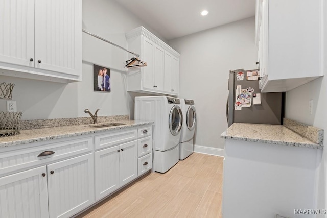 clothes washing area with sink, cabinets, washer and dryer, and light wood-type flooring