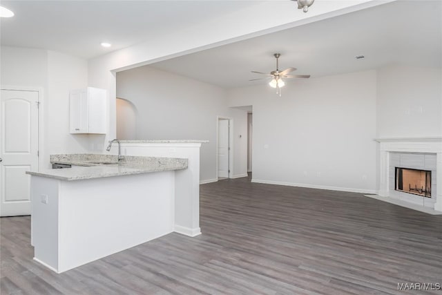 kitchen with sink, light stone counters, ceiling fan, a tiled fireplace, and white cabinets