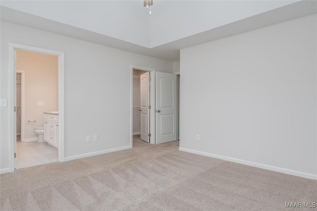 unfurnished bedroom with connected bathroom, a walk in closet, light colored carpet, and a closet