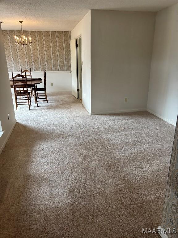 carpeted empty room featuring an inviting chandelier and a textured ceiling