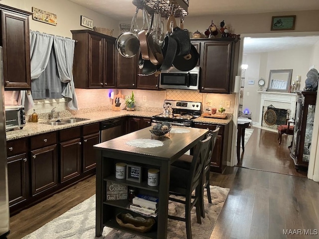 kitchen with dark brown cabinetry, dark wood-style floors, a sink, stainless steel appliances, and backsplash