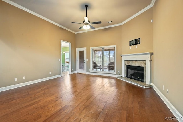 unfurnished living room with crown molding, dark wood-type flooring, ceiling fan, a high ceiling, and a tiled fireplace