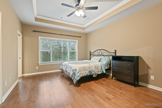 bedroom with a tray ceiling, ornamental molding, light hardwood / wood-style floors, and ceiling fan