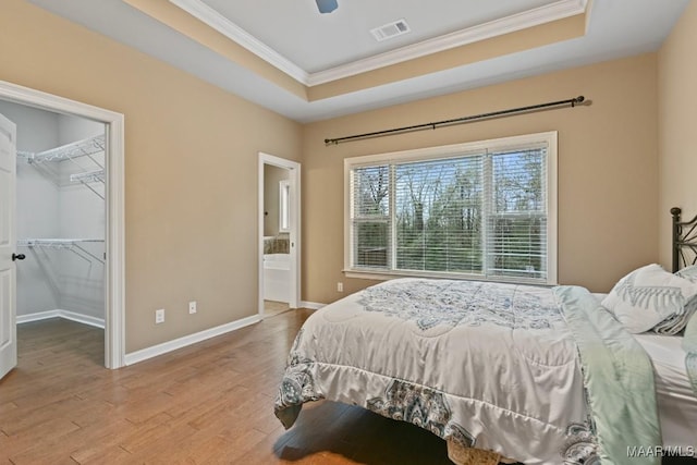 bedroom with crown molding, a tray ceiling, a walk in closet, and light hardwood / wood-style floors