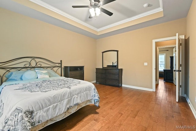 bedroom featuring wood-type flooring, ornamental molding, a raised ceiling, and ceiling fan