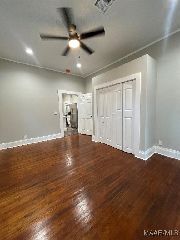 unfurnished bedroom with stainless steel refrigerator with ice dispenser, ornamental molding, dark wood-type flooring, and a closet