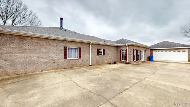 back of house with a garage, driveway, brick siding, and roof with shingles