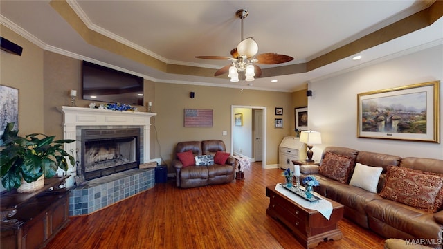 living room featuring crown molding, a raised ceiling, a brick fireplace, ceiling fan, and wood finished floors