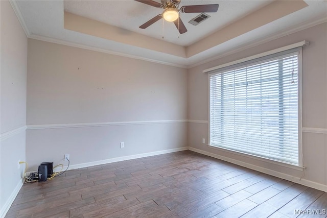 unfurnished room with a raised ceiling, visible vents, baseboards, and wood finished floors