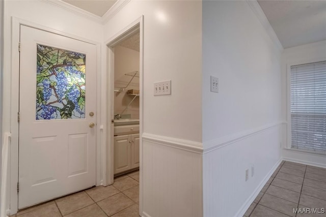 interior space with a wainscoted wall, crown molding, a sink, and light tile patterned floors