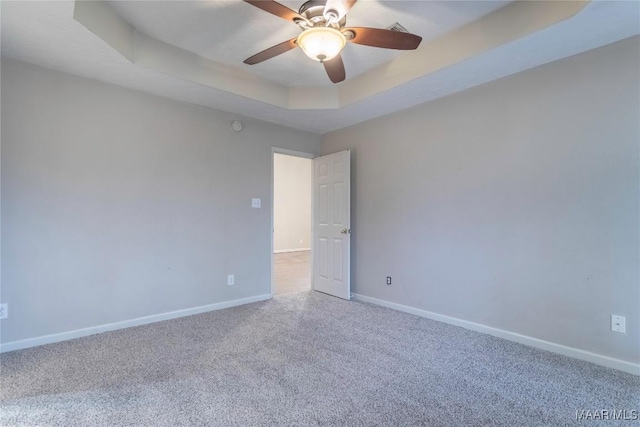 carpeted spare room featuring ceiling fan, a tray ceiling, and baseboards