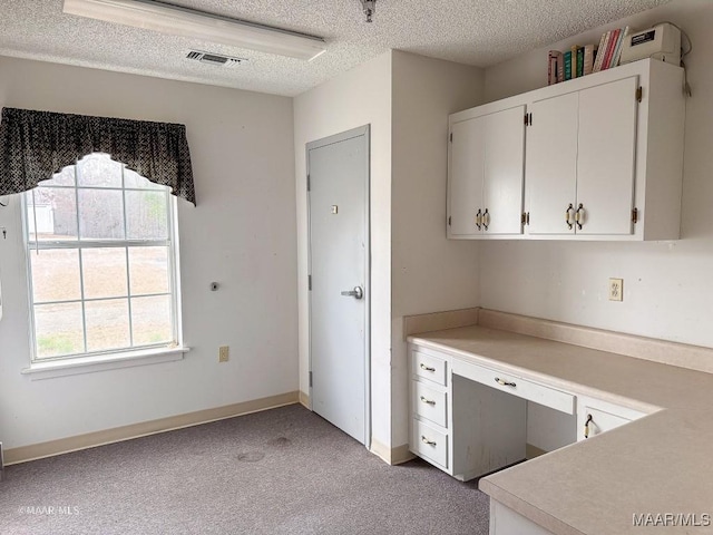 kitchen featuring a textured ceiling, built in desk, light colored carpet, and white cabinets