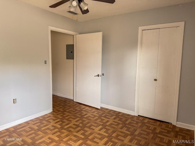 unfurnished bedroom featuring ceiling fan, a closet, electric panel, and dark parquet floors