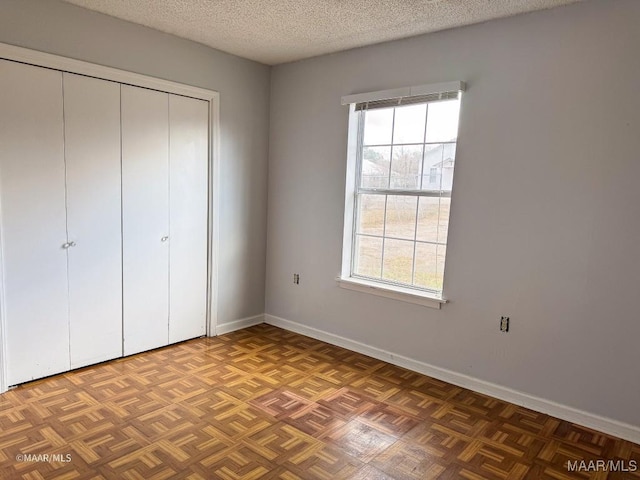 unfurnished bedroom featuring multiple windows, dark parquet floors, and a textured ceiling