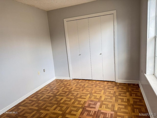 unfurnished bedroom with dark parquet flooring, a closet, and a textured ceiling