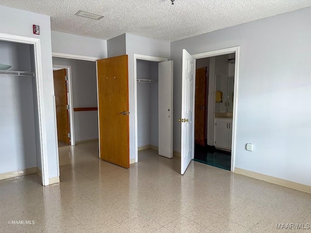 unfurnished bedroom with two closets, a textured ceiling, and ensuite bath