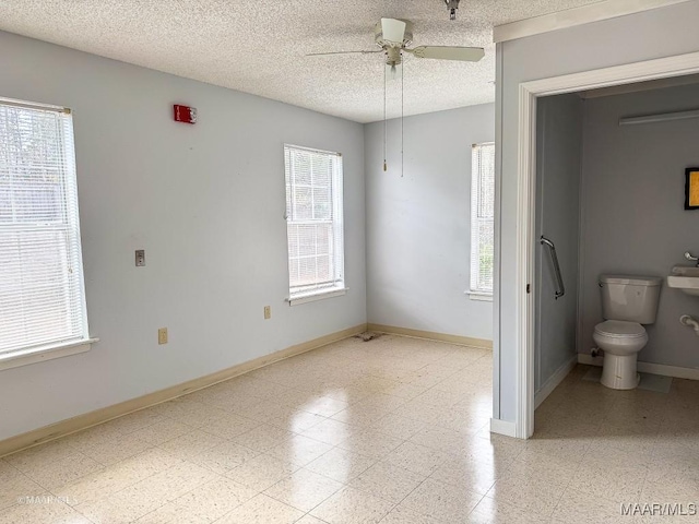 interior space featuring ceiling fan, a textured ceiling, toilet, and a healthy amount of sunlight