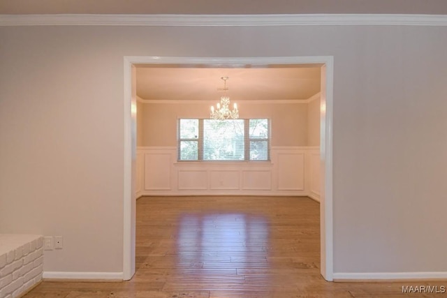 spare room with wainscoting, an inviting chandelier, wood finished floors, and crown molding