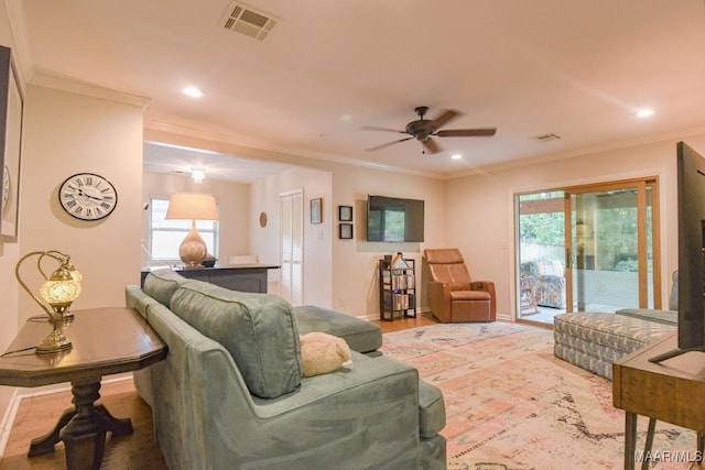living room featuring visible vents, a healthy amount of sunlight, ornamental molding, and a ceiling fan