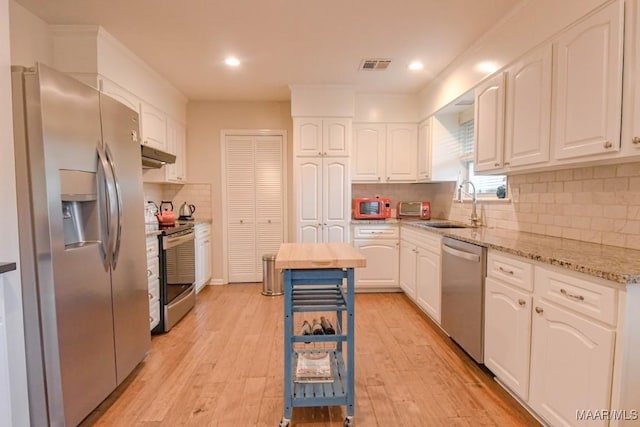 kitchen with visible vents, a sink, under cabinet range hood, appliances with stainless steel finishes, and white cabinets