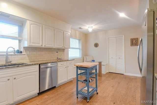 kitchen with stone countertops, a sink, stainless steel appliances, tasteful backsplash, and light wood-type flooring