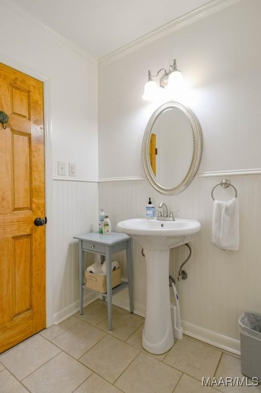 bathroom with tile patterned flooring, a wainscoted wall, crown molding, and a sink