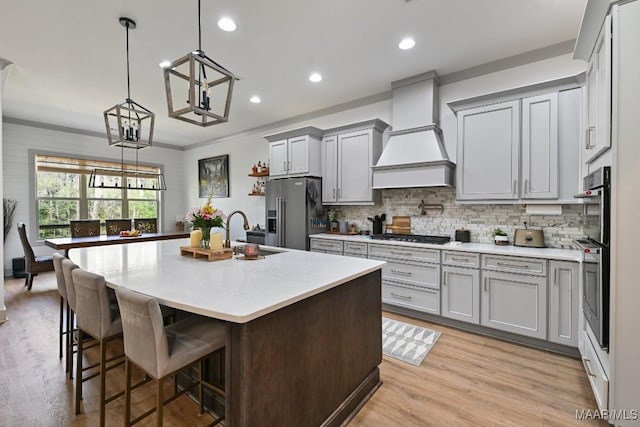 kitchen featuring sink, hanging light fixtures, stainless steel appliances, custom range hood, and an island with sink