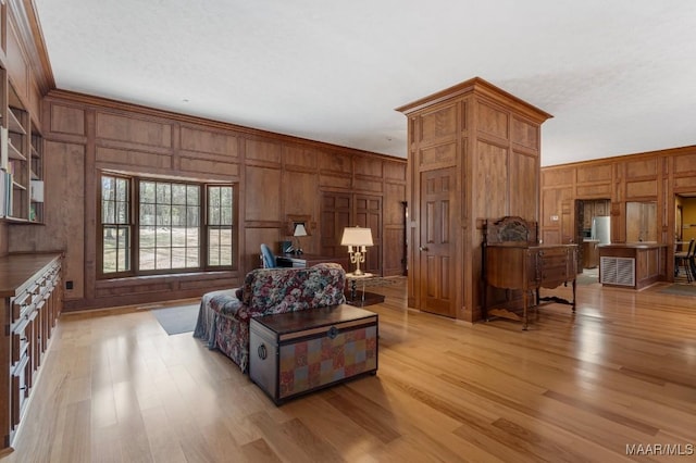 living room with crown molding, wooden walls, and light hardwood / wood-style floors