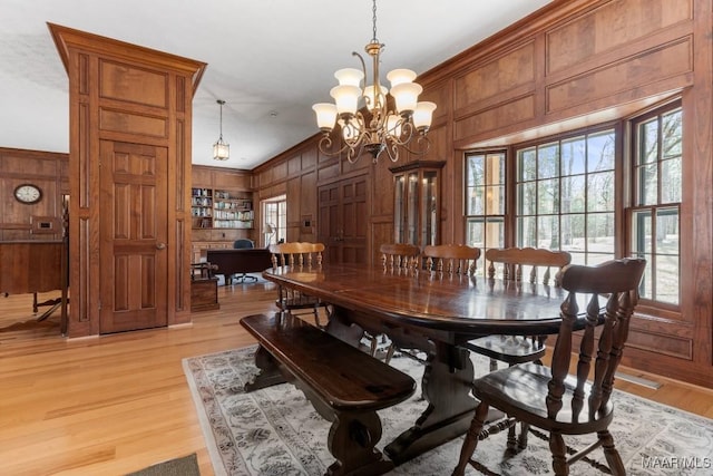 dining space with crown molding, light hardwood / wood-style flooring, an inviting chandelier, built in shelves, and wood walls