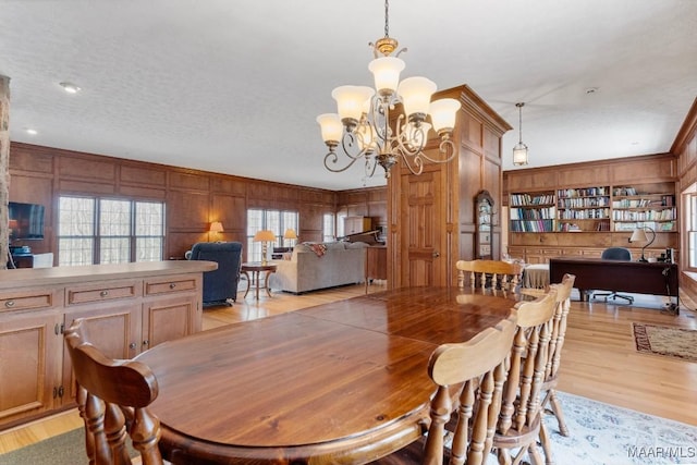 dining room featuring an inviting chandelier, light hardwood / wood-style flooring, a textured ceiling, wooden walls, and built in features