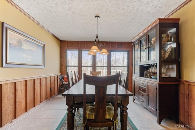 tiled dining room with crown molding, an inviting chandelier, a textured ceiling, and wood walls