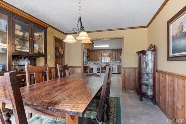 dining area with wood walls, a textured ceiling, ornamental molding, a notable chandelier, and tile patterned flooring