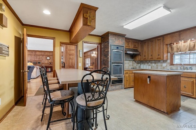 kitchen featuring a kitchen island, tasteful backsplash, sink, crown molding, and stainless steel double oven