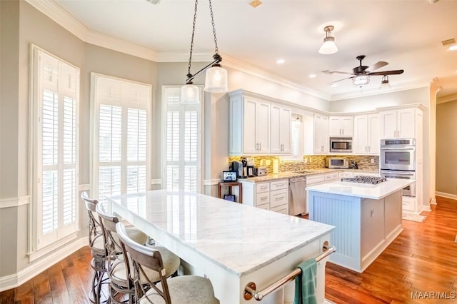 kitchen with pendant lighting, stainless steel appliances, white cabinets, a kitchen island, and dark hardwood / wood-style flooring