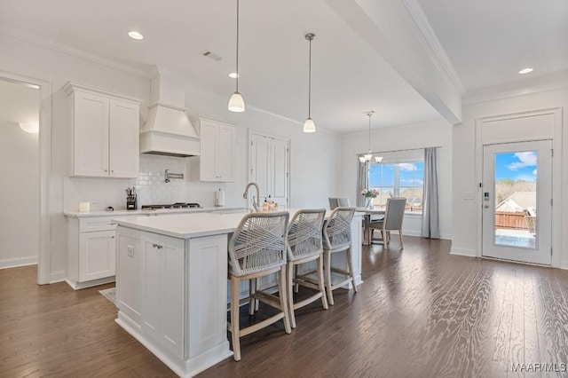 kitchen with premium range hood, an island with sink, hanging light fixtures, and white cabinets