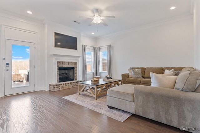 living room with crown molding, a brick fireplace, dark wood-type flooring, and ceiling fan