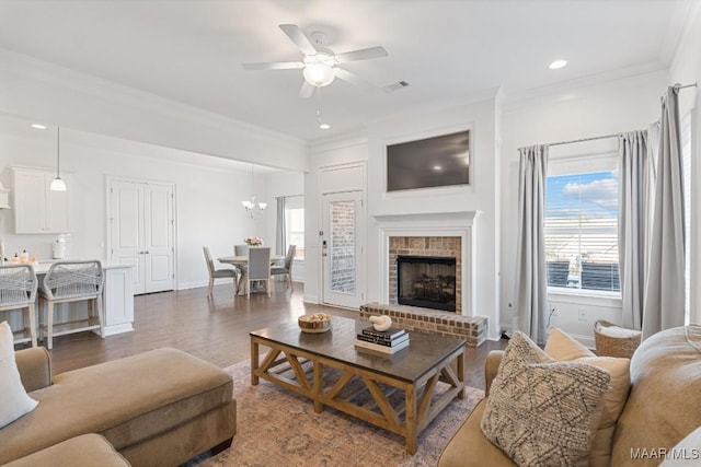 living room featuring a brick fireplace, ceiling fan with notable chandelier, ornamental molding, and dark hardwood / wood-style floors