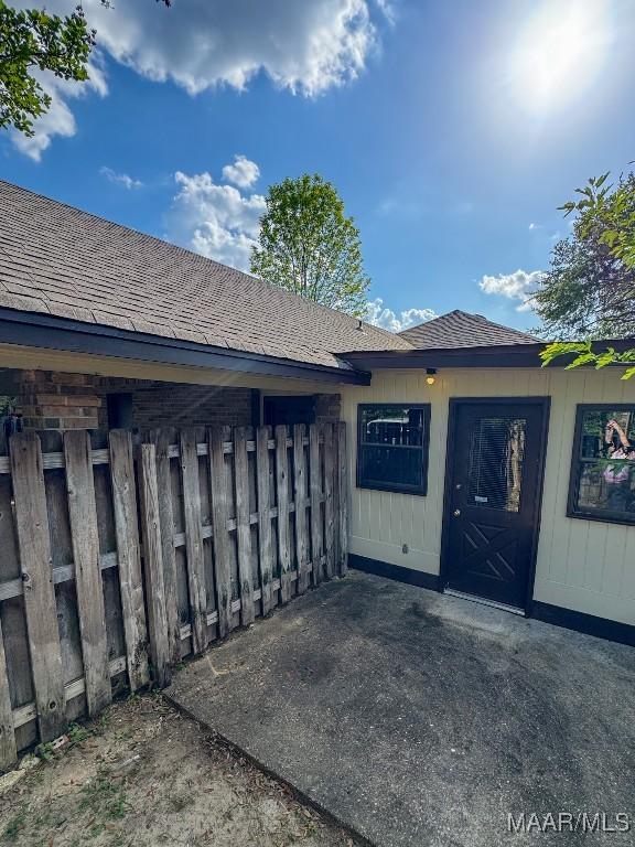 view of exterior entry with fence and roof with shingles