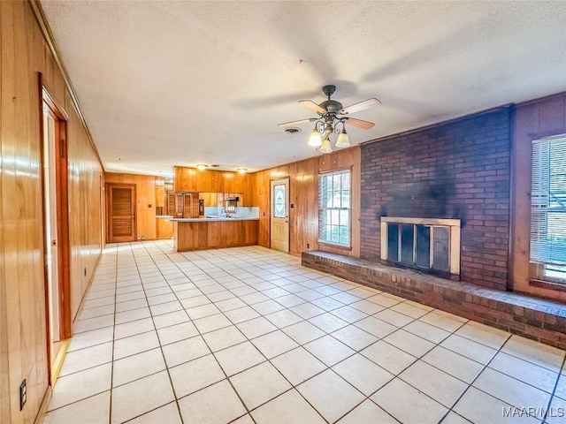 unfurnished living room with a brick fireplace, light tile patterned floors, a textured ceiling, and wood walls